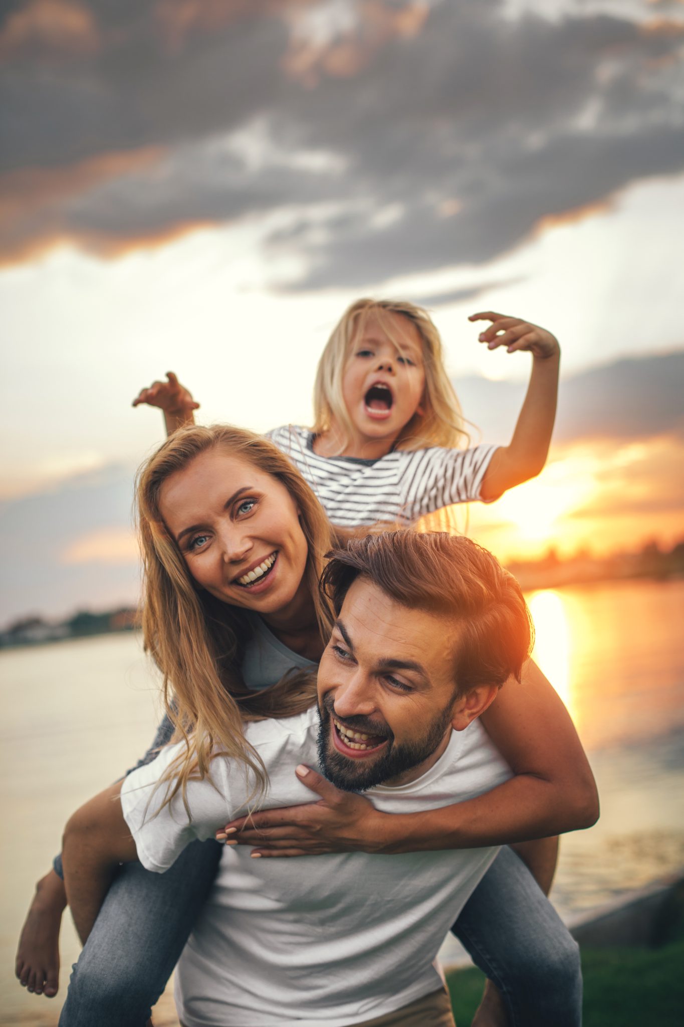 Portrait of happy unshaven husband spending tie with cheerful wife and satisfied female child in nature
